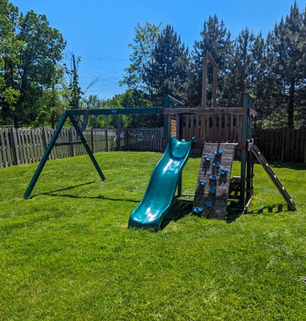 Children's wooden playset with slide and climbing wall in backyard.
