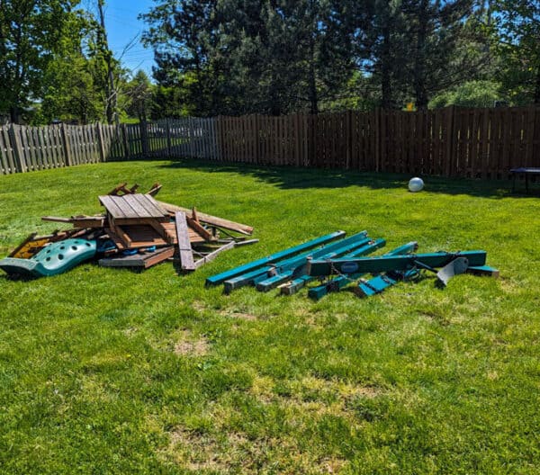 Disorganized backyard with wooden and plastic debris on green grass.