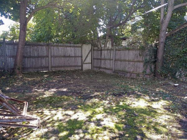 Empty backyard with trees and wooden fence, ideal for landscaping.