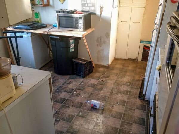 Cluttered kitchen with trash and appliances in disarray.