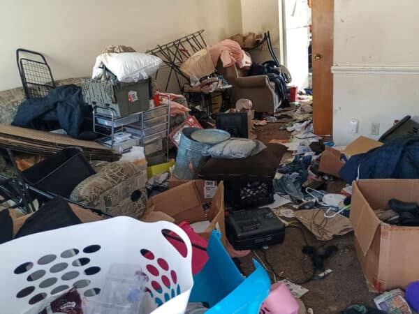 Cluttered room with furniture, boxes, and debris after damage.