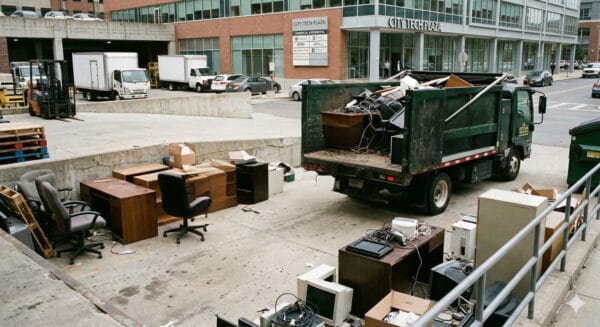 Junk removal truck with office furniture and electronics in urban setting.