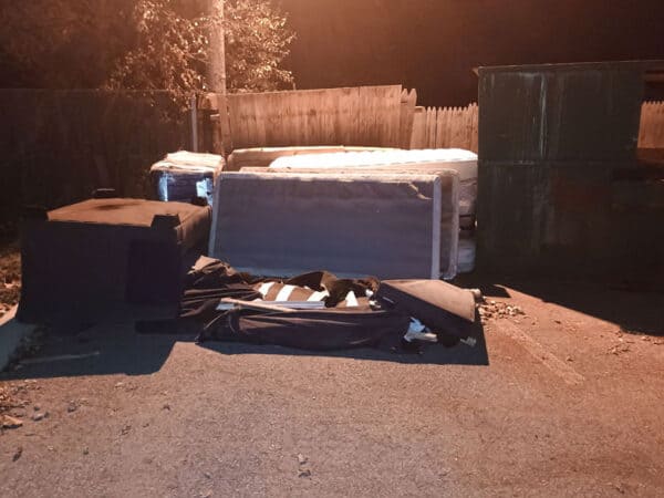Outdoor storage area with mattresses, boxes, and debris at night.