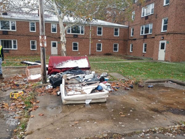 Damaged mattress and debris outside apartment complex in fall.