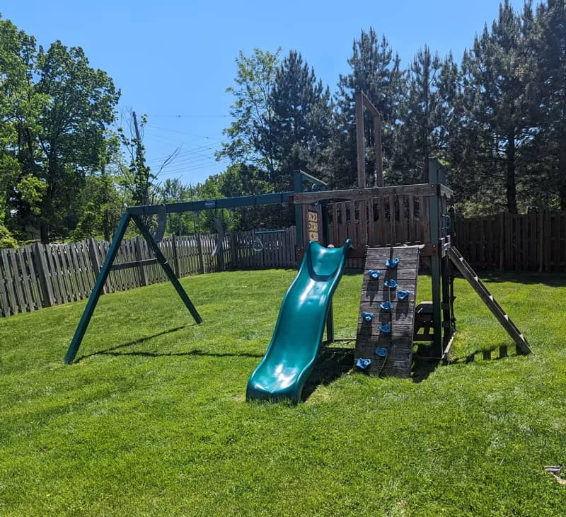 Outdoor playground with slide, climbing wall, and swing set in backyard.